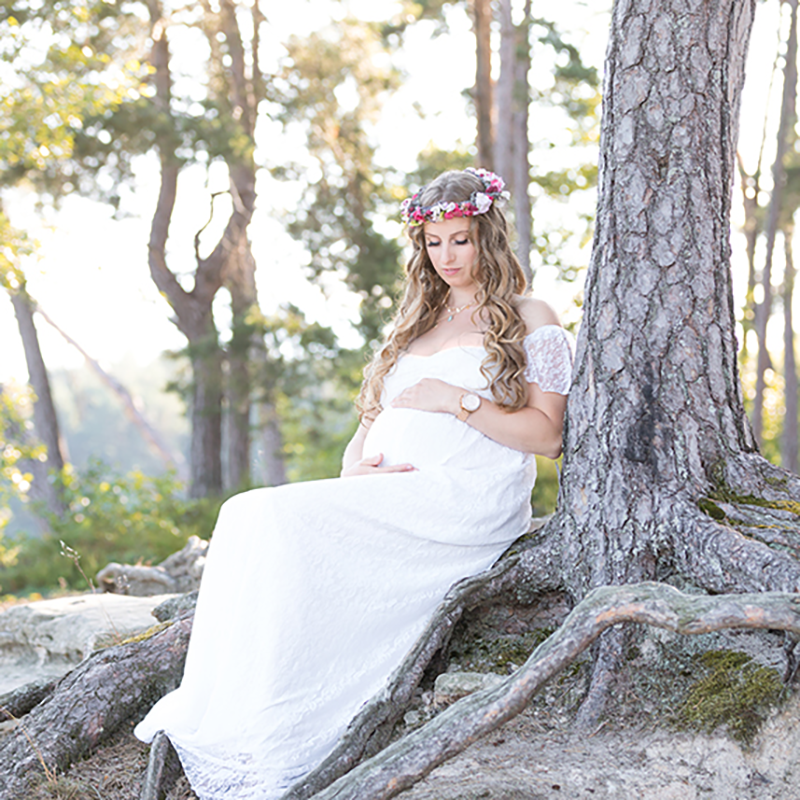 Schwangere Frau im Wald mit Blumenkranz und weißem Kleid.